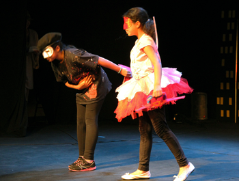 A young child wearing all black holds the hand of another child wearing a white and pink dress